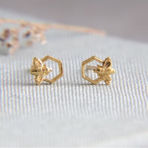 Peut inclure: Une paire de boucles d'oreilles dorées en forme d'abeille dans un hexagone.