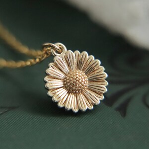 Puede incluir: Un collar dorado con una cadena delicada y un dije en forma de margarita. El dije de margarita tiene un centro texturizado y p&eacute;talos.