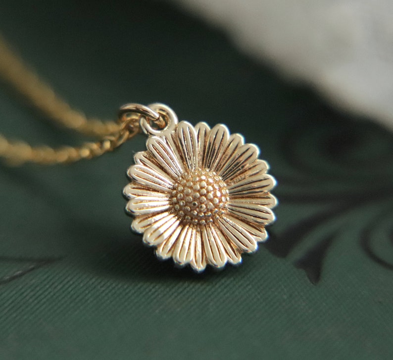 Puede incluir: Un collar dorado con una cadena delicada y un dije en forma de margarita. El dije de margarita tiene un centro texturizado y p&eacute;talos.