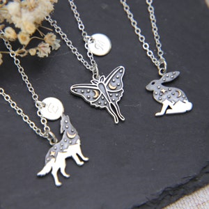 Peut inclure: Quatre colliers en argent avec différents pendentifs : un loup, un papillon de nuit, un lapin et une lettre « B ». Chaque pendentif est orné d’un motif de lune et d’étoiles avec des accents dorés.
