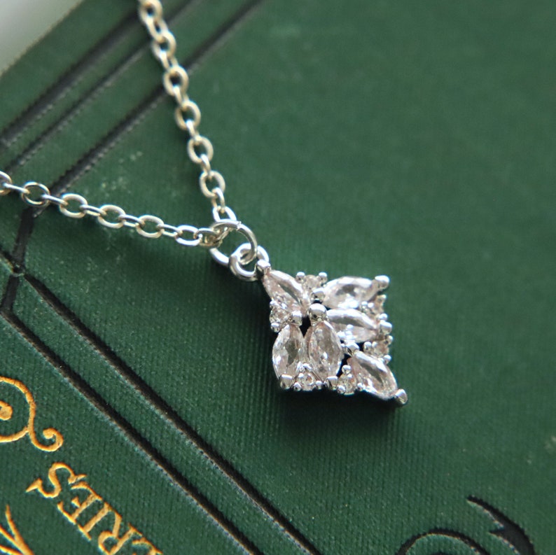 May include: A silver necklace with a delicate chain and a pendant featuring a cluster of clear, sparkling stones arranged in a geometric shape.