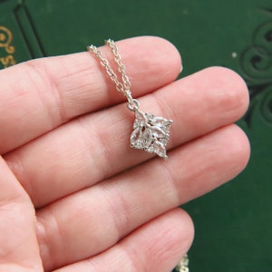May include: A silver necklace with a delicate pendant featuring a cluster of clear, faceted stones arranged in a flower-like design.