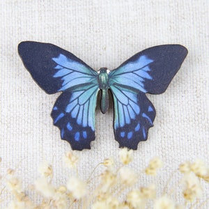 K&ouml;nnte beinhalten: Ein Holzschmetterling mit einem detaillierten blau-schwarzen Fl&uuml;gelmuster. Der Schmetterling hat einen dunkelblauen K&ouml;rper und Fl&uuml;gel mit verschiedenen Blaut&ouml;nen. Die Fl&uuml;gel sind ausgebreitet und zeigen das komplizierte Design.