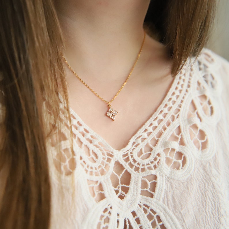 May include: A delicate gold chain necklace with a small, sparkling, diamond-shaped pendant.