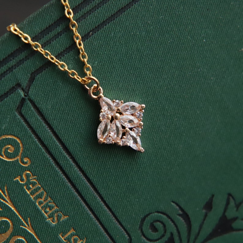 May include: A gold chain necklace with a delicate pendant featuring a cluster of clear cubic zirconia stones arranged in a flower shape.