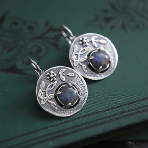 May include: A pair of silver earrings featuring a floral design and a dark blue gemstone at the centre of each earring.