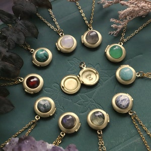 Puede incluir: Una colección de 12 collares con medallones de oro adornados con piedras preciosas de diferentes colores. Los medallones están abiertos para revelar un interior vacío. Los medallones están dispuestos en círculo sobre una superficie verde.