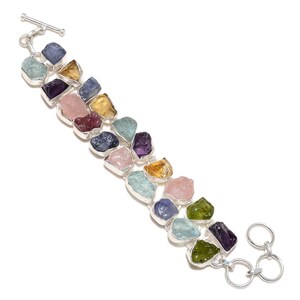 May include: A silver bracelet featuring a row of colourful, rough-cut gemstones. The stones include amethyst, aquamarine, citrine, rose quartz, and green aventurine.