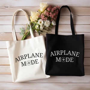 May include: Two tote bags, one white and one black, with the text "AIRPLANE MODE" and a small airplane symbol printed on them. The bags are made of canvas and have a simple design.