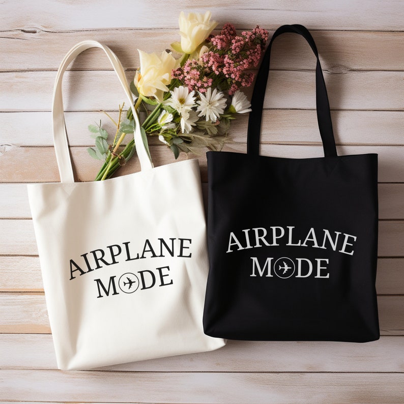 May include: Two tote bags, one white and one black, with the text "AIRPLANE MODE" and a small airplane symbol printed on them. The bags are made of canvas and have a simple design.