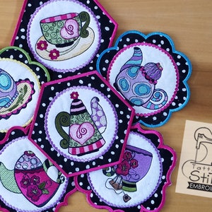May include: Six embroidered teacup and teapot designs on fabric circles. The designs are colourful and feature polka dots, hearts, and swirls. The circles are surrounded by black fabric with white polka dots.