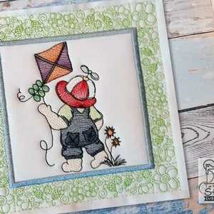 May include: Embroidered design of a child wearing a red hat and overalls holding a kite with a green clover. The design is surrounded by a green and white floral border.