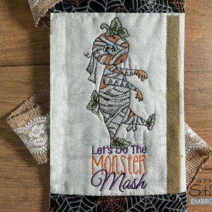 May include: Embroidered kitchen towel with a mummy pumpkin design and the text "Let's Do The Monster Mash".