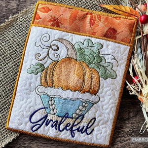 Może przedstawiać: Haftowany uchwyt na garnek do kuchni z jesiennym motywem. Prezentuje dynię w niebieskim i białym koszyku z zielonymi liśćmi i słowem "Grateful" w ozdobnym pismie.