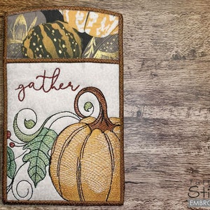May include: Embroidered design featuring a pumpkin with green leaves and the word "gather" in a brown font. The design is on a white background with a brown border.