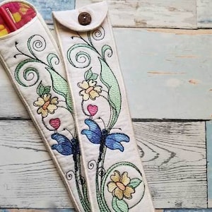 Puede incluir: Dos estuches de tela blanca con diseños florales bordados, incluyendo mariposas, corazones y flores. Los estuches son para guardar artículos como agujas de tejer o palillos chinos.