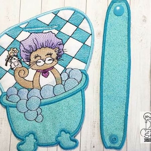 May include: Embroidered design of a cat in a shower cap taking a bath in a blue tub with bubbles. The design is on a white and blue checkered background. There is a matching blue strap with a snap closure.