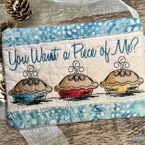 May include: A beige fabric pot holder with blue trim features embroidered text that reads "You Want a Piece of Me?" and three embroidered pies with steam rising from the top.