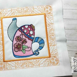 May include: Embroidered design of a whimsical teapot with pink, blue, and white details. The teapot is surrounded by a yellow frame with a floral pattern.