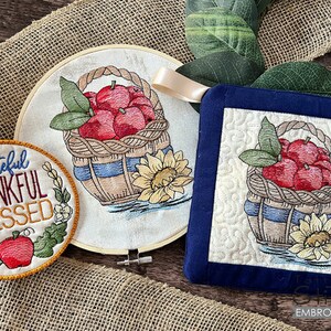 Puede incluir: Un juego de dos toallas de cocina bordadas con fondo azul y diseño blanco. El diseño presenta una cesta de manzanas rojas con girasoles y el texto "Grateful Thankful Blessed".