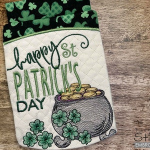 May include: A white quilted pot holder with green shamrocks and the text "Happy St. Patrick's Day". A gray pot with gold coins is embroidered on the bottom.