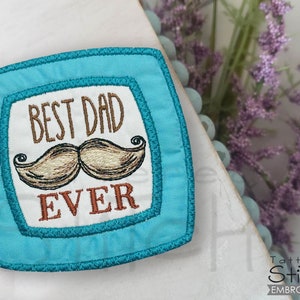 Puede incluir: Un parche cuadrado azul turquesa con fondo blanco y texto bordado que dice "Best Dad Ever" con un bigote marrón debajo.