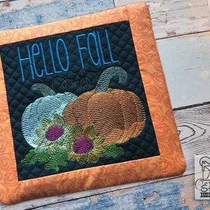 May include: Embroidered pot holder with an orange and brown border. The centre features a black background with the text "Hello Fall" in blue embroidery. Two pumpkins and sunflowers are embroidered in the bottom half of the design.