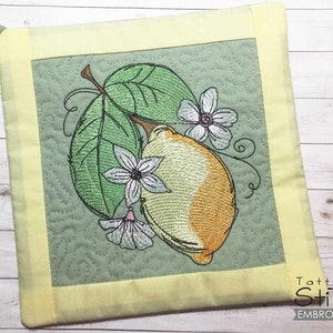 May include: Embroidered square potholder featuring a lemon with green leaves and white flowers. The design is on a light green background with a yellow border and a hanging loop. The text "Tattered Stitch Embroideries" is in the bottom right corner.