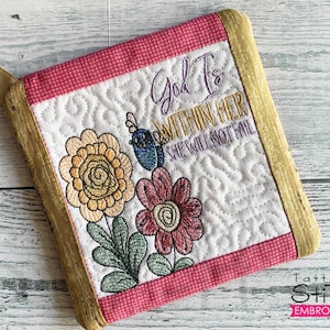 May include: A pink and gold quilted pot holder with embroidered flowers and the text "God Is Within Her She Will Not Fail".