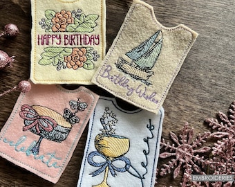 May include: Four felt gift tags with embroidered designs. The first tag is yellow with a floral design and the text "Happy Birthday". The second tag is beige with a sailboat design and the text "Birthday Wishes". The third tag is pink with a cake design and the text "Celebrate". The fourth tag is white with a cocktail glass design and the text "Cheers".
