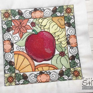 Pode incluir: Desenho bordado com uma maçã vermelha, folhas de outono, abóboras e girassóis em uma moldura quadrada. O desenho é perfeito para um projeto de artesanato de outono.