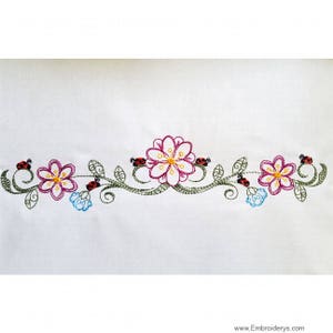 Könnte beinhalten: Gestickte Bordüre mit rosa und gelben Blumen, grünen Blättern und roten Marienkäfern.
