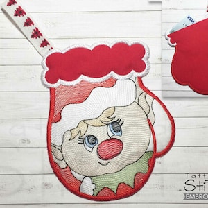 May include: Red and white felt Christmas stocking with an embroidered elf face. The stocking has a loop for hanging and a pocket on the back.