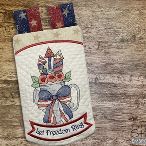 May include: A white quilted fabric ring with a red, white, and blue fireworks design and the text "Let Freedom Ring".