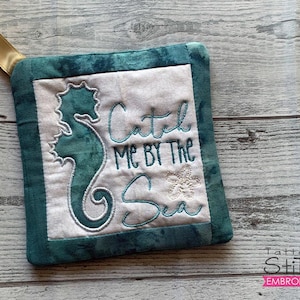 May include: A teal blue and white pot holder with a seahorse and the text "Catch Me By The Sea".