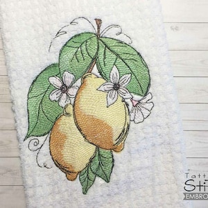 Könnte beinhalten: Gestickte Darstellung von zwei Zitronen mit grünen Blättern und weißen Blüten. Das Design befindet sich auf einem weißen Handtuch mit dem Text "Tattered Stitch Embroideries" in der rechten unteren Ecke.
