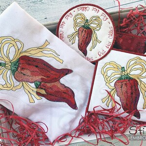 Op de afbeelding: Geborduurde keukendoek met een rood chilipeperontwerp. De handdoek heeft een strik en de tekst "Red Hot Chillies - Red Hot Chillies".