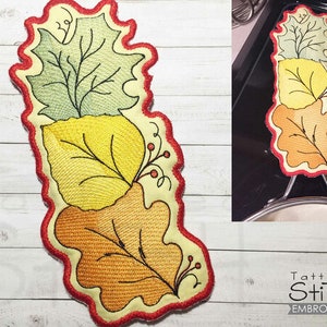 Puede incluir: Un agarrador de olla en forma de hoja roja, amarilla y verde con un contorno rojo. El agarrador de olla está diseñado para parecerse a tres hojas apiladas una encima de la otra. Las hojas están bordadas con un diseño detallado. El agarrador de olla es una excelente manera de proteger tus manos de las superficies calientes.