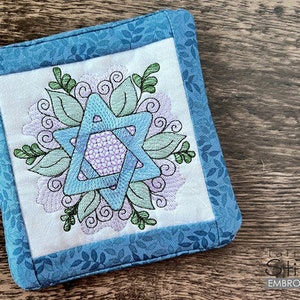 May include: A blue and green embroidered Star of David with floral designs on a blue and white fabric coaster.