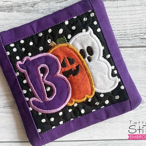 May include: Purple and black Halloween-themed pot holder with a large purple letter "B", two orange pumpkins, and a white ghost. The text "Tattered Stitch Embroideries" is visible in the lower right corner.