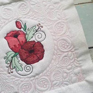 May include: Embroidered design of red poppies with green leaves and swirls on a white fabric background. The fabric has a quilted pattern of small circles.
