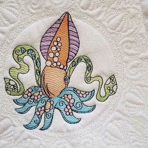 May include: Embroidered design of a colorful squid with a purple, orange, and white head and blue, green, and pink tentacles. The squid is surrounded by a circle of green leaves and pink flowers.
