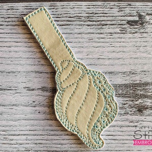 May include: A beige fabric bookmark with a blue embroidered design. The design is a stylised swirl with a scalloped edge.