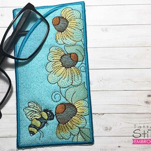 May include: A blue and white embroidered eyeglass case with a floral design and a bee. The case is made by Tattered Stitch Embroideries.