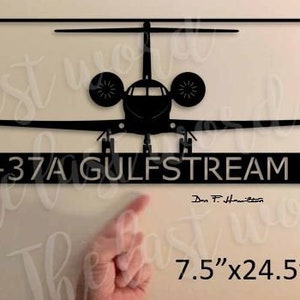 May include: Black metal wall art of a Gulfstream V private jet with the text "C-37A GULFSTREAM V" and the signature "Don T. Hamilton". The art measures 7.5 inches by 24.5 inches.