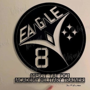 May include: Black metal sign with the words "EAGLE 8" and "MSG TALDO ACADEMY MILITARY TRAINER" in white lettering. The sign is 18 inches by 16.5 inches.