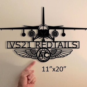 May include: Black metal wall art featuring a silhouette of a plane with the text "VS21 REDTAILS" and an anchor with wings. The art measures 11 inches by 20 inches.