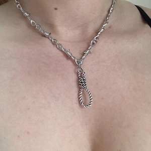 Puede incluir: Un collar de plata con una cadena de alambre de púas y un colgante de cuerda retorcida.