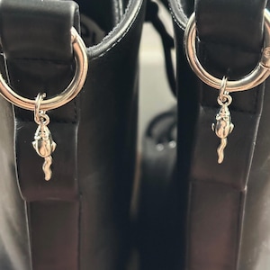 May include: A pair of black leather boots featuring silver metal rings and mouse-shaped charms. The boots have a classic lace-up design. The charms add a quirky detail to the boots, suggesting a gothic or alternative style. The boots are made of leather.