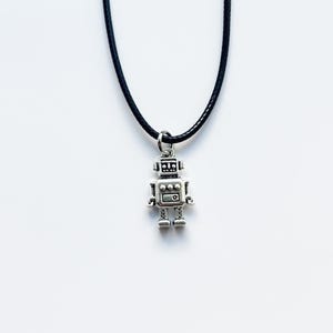 May include: A silver-colored robot pendant necklace with a black cord. The robot charm has a detailed design with a square body, rectangular chest, and small legs. The text "Pissy Prints" is at the bottom.